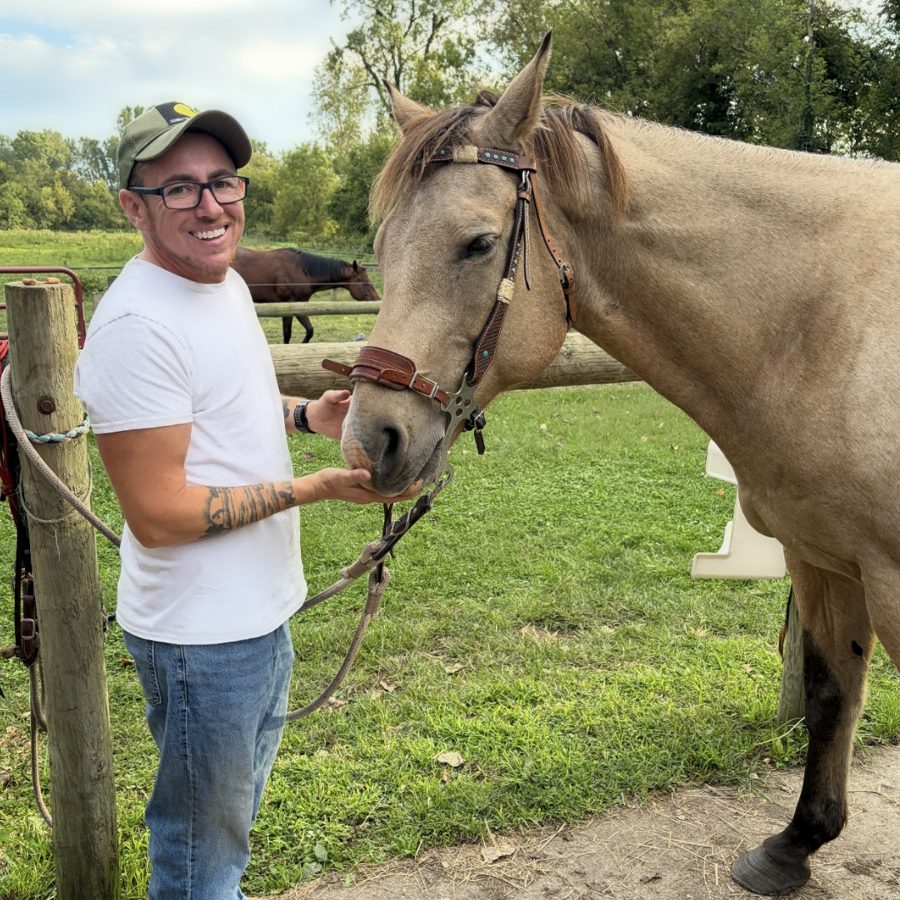 Smiling at a farm, petting a buckskin horse